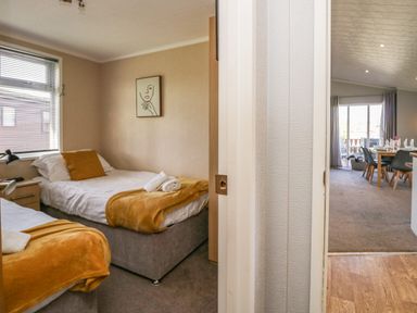 A bedroom with two single beds and orange blankets next to a dining area with a set table at Lakeside 20 in Warton near Carnforth
