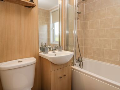 A bathroom with a toilet sink with soap dispenser and a bathtub with shower at Lakeside 20 in Warton near Carnforth