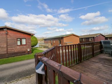A wooden deck with patio furniture and wooden cabins under a partly cloudy sky at Lakeside 20 in Warton near Carnforth