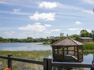 A lakeside view with a wooden gazebo on the water and cabins in the background at Lakeside 20 in Warton near Carnforth