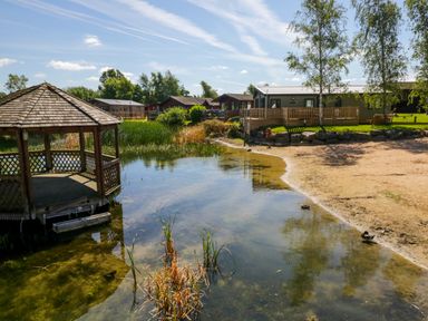 A lakeside area with a wooden gazebo dock sandy shore and houses in the background at Lakeside 20 in Warton near Carnforth
