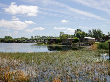 A lake with reeds and wooden cabins along the shore at Lakeside 20 in Warton near Carnforth
