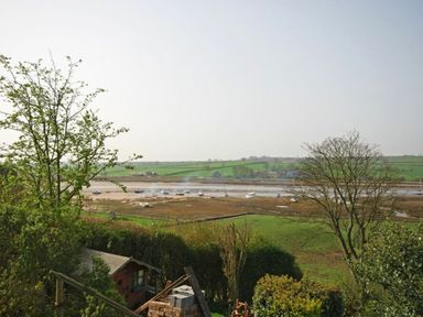 A view of a river with boats and green fields in the background at Riverbank Cottage in Alnmouth