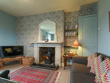 A living room with a fireplace TV sofa with pillows and a side table with a lamp at Riverbank Cottage in Alnmouth