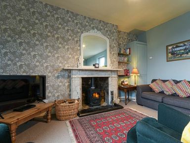A living room with a fireplace a wooden coffee table and a sofa with patterned cushions at Riverbank Cottage in Alnmouth
