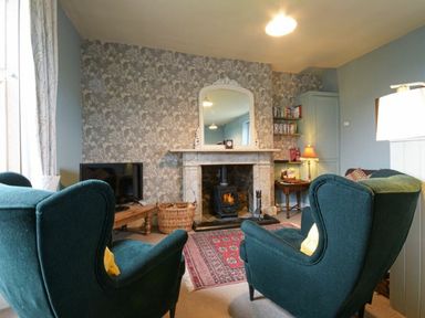 A living room with two green armchairs facing a fireplace with a mirror above at Riverbank Cottage in Alnmouth