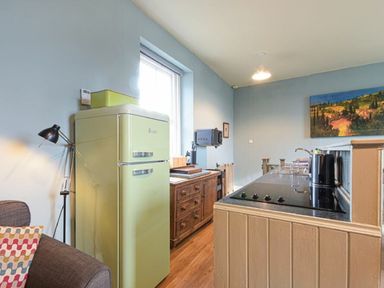 A kitchen with a green refrigerator a wooden cabinet a window and a stovetop at Riverbank Cottage in Alnmouth