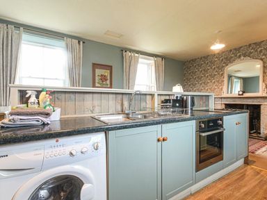 A kitchen with washing machine sink oven and countertop at Riverbank Cottage in Alnmouth