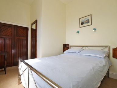 A bedroom with a double bed next to a wooden wardrobe and a wall mirror at Riverbank Cottage in Alnmouth
