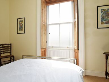 A bedroom with a bed near a window with wooden shutters and framed pictures on the walls at Riverbank Cottage in Alnmouth