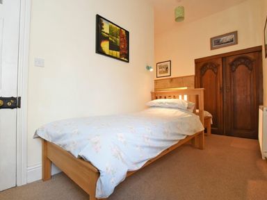 A bedroom with a single wooden bed with blue floral bedding a wooden wardrobe and framed pictures on the walls at Riverbank Cottage in Alnmouth