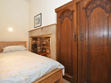 A bedroom with a wooden bed near a stone fireplace and a carved wooden wardrobe at Riverbank Cottage in Alnmouth
