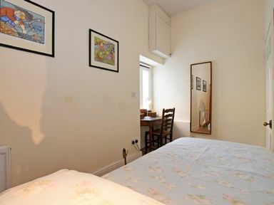 A bedroom with a bed a wooden desk and chair a mirror on the wall and framed pictures at Riverbank Cottage in Alnmouth