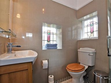 A bathroom with a toilet with wooden seat a sink with cabinet and stained glass windows at Riverbank Cottage in Alnmouth