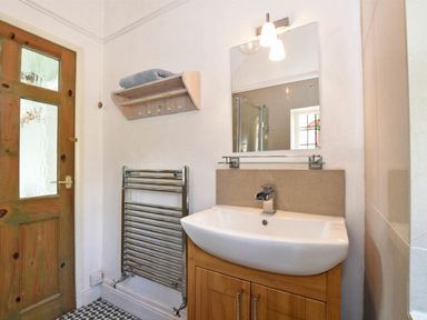 A bathroom with a wooden door a towel rack a sink with a wooden cabinet a mirror and a wall shelf with a towel at Riverbank Cottage in Alnmouth