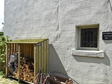 A storage area with firewood and bags next to a window on a building exterior at Riverbank Cottage in Alnmouth
