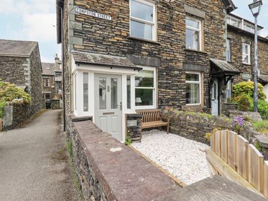 Stone built terraced houses with a small gravel front yard and wooden benches on Compston Street at Woolly End Cottage in Ambleside