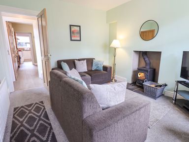 A living room with brown sofas a wood stove and a lamp at Woolly End Cottage in Ambleside