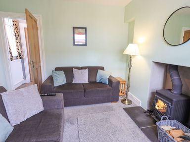 A living room with two sofas a floor lamp a wood burning stove and a basket of firewood at Woolly End Cottage in Ambleside