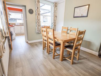 A dining room with a wooden table six chairs wall clock and a window at Woolly End Cottage in Ambleside