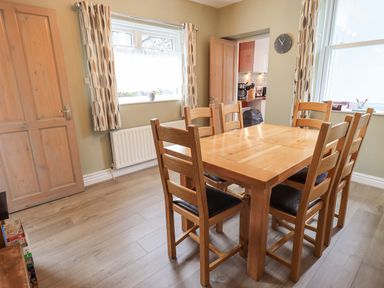 A dining room with a wooden table and six chairs near two windows at Woolly End Cottage in Ambleside