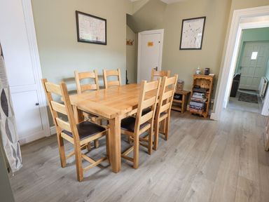 A dining room with a wooden table and six chairs and framed maps on the walls at Woolly End Cottage in Ambleside