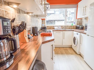 A kitchen with wooden countertops washing machine toaster coffee maker and window at Woolly End Cottage in Ambleside