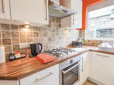 A kitchen with a gas stove oven black kettle black toaster and window at Woolly End Cottage in Ambleside