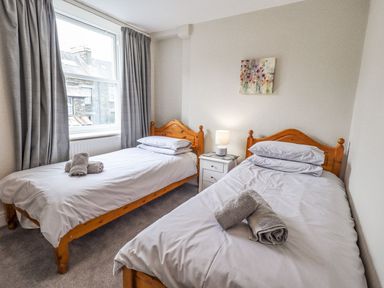 A bedroom with two single wooden beds white bedding and towels on the beds at Woolly End Cottage in Ambleside