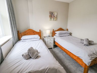 A bedroom with two single beds wooden headboards a nightstand and a lamp at Woolly End Cottage in Ambleside