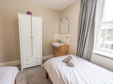 A bedroom with a bed and rolled towels next to a window and a white wardrobe with a sink and mirror in the corner at Woolly End Cottage in Ambleside