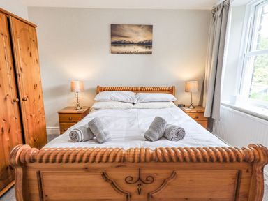 A bedroom with a wooden bed and wardrobe two bedside tables with lamps and a window at Woolly End Cottage in Ambleside