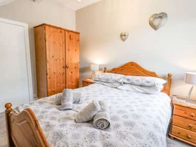 A bedroom with a wooden bed a wardrobe bedside tables and lamps at Woolly End Cottage in Ambleside