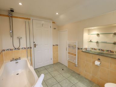 A bathroom with a bathtub with shower and towel radiator near a door with shelves on the wall at Woolly End Cottage in Ambleside
