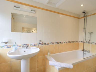 A bathroom with a pedestal sink mirror and a bathtub with a shower screen at Woolly End Cottage in Ambleside