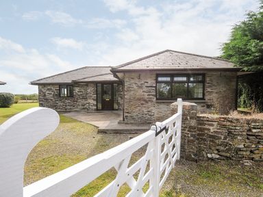 A stone house with a tiled roof and a white gate in front at The Old Forge in Trerulefoot