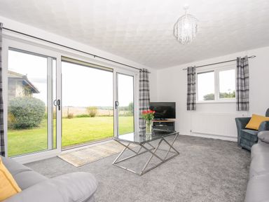 A living room with glass coffee table and sliding doors opening to a garden at The Old Forge in Trerulefoot