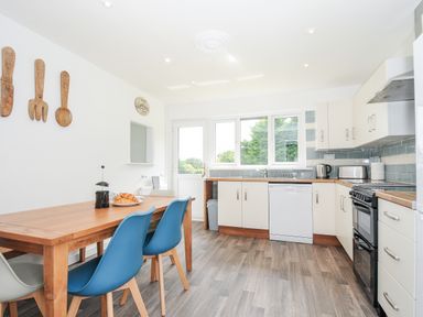 A kitchen with a wooden dining table and blue chairs and white cabinets with appliances at The Old Forge in Trerulefoot