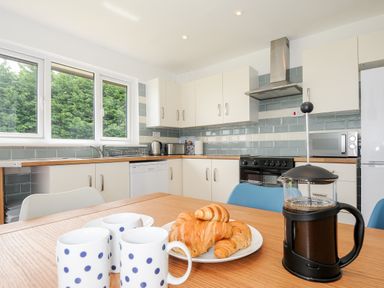 A kitchen with cabinets countertop and appliances with a table holding croissants mugs and a French press at The Old Forge in Trerulefoot