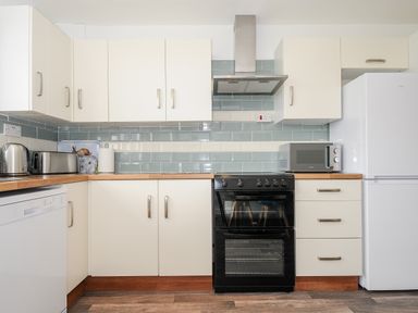 A kitchen with white cabinets a black stove a white refrigerator microwave toaster and kettle at The Old Forge in Trerulefoot