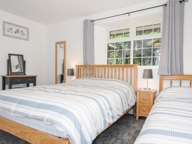 A bedroom with two beds a window bedside table lamps a dressing table and a full length mirror at The Old Forge in Trerulefoot