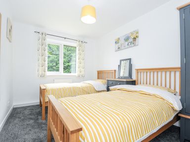 A bedroom with two single beds with yellow striped bedding a window with patterned curtains and a wardrobe at The Old Forge in Trerulefoot