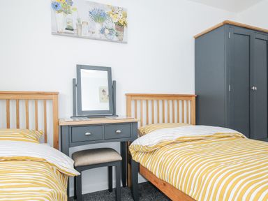 A bedroom with two single beds with yellow striped bedding a dressing table with mirror and stool and a wardrobe at The Old Forge in Trerulefoot