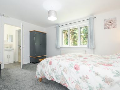 A bedroom with a bed covered with floral bedding a wardrobe a door leading to a bathroom and a window with curtains at The Old Forge in Trerulefoot