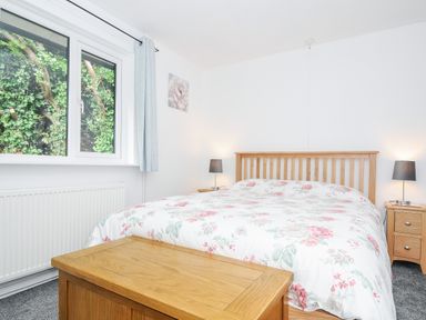 A bedroom with a wooden bed with floral bedding two bedside tables with lamps a window with curtains and a wooden chest at the foot of the bed at The Old Forge in Trerulefoot