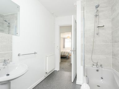 A bathroom with a sink, bathtub with shower, and an open door leading to a bedroom at The Old Forge in Trerulefoot