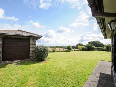 A backyard with a garage a lawn and bushes at The Old Forge in Trerulefoot