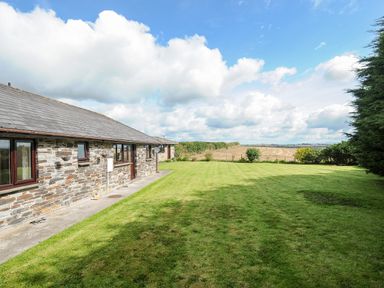 A stone house with a grassy lawn and farmland in the background at The Old Forge in Trerulefoot