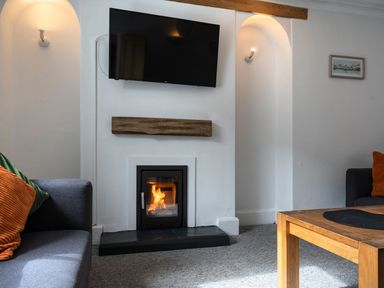 A living room with a fireplace a wall mounted television two sofas and a wooden table at Ayr Farmhouse in St Ives