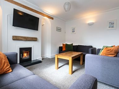 A living room with grey sofas and wooden coffee table a fireplace and a wall-mounted tv at Ayr Farmhouse in St Ives